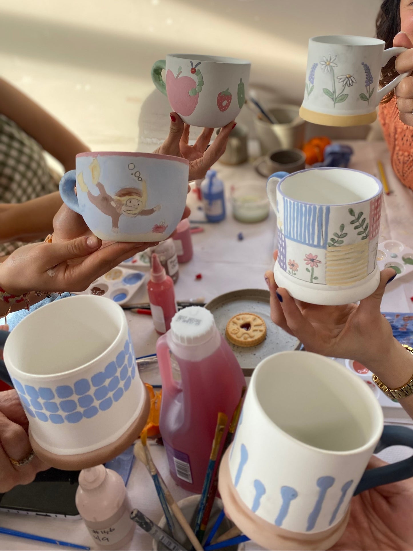 people holding their painted mugs in a pottery painting class